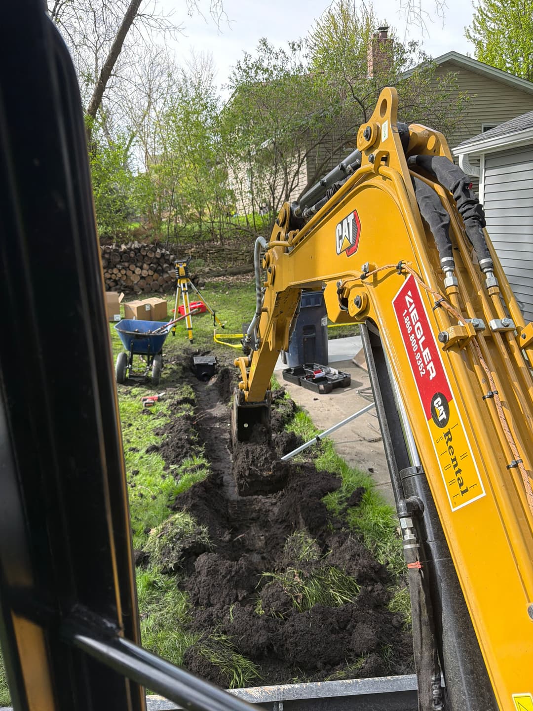 Excavator digging a trench in a residential yard for landscaping projects.
