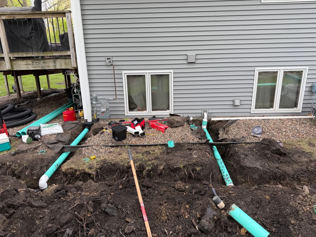 Residential plumbing installation with exposed PVC pipes and construction tools near a house.