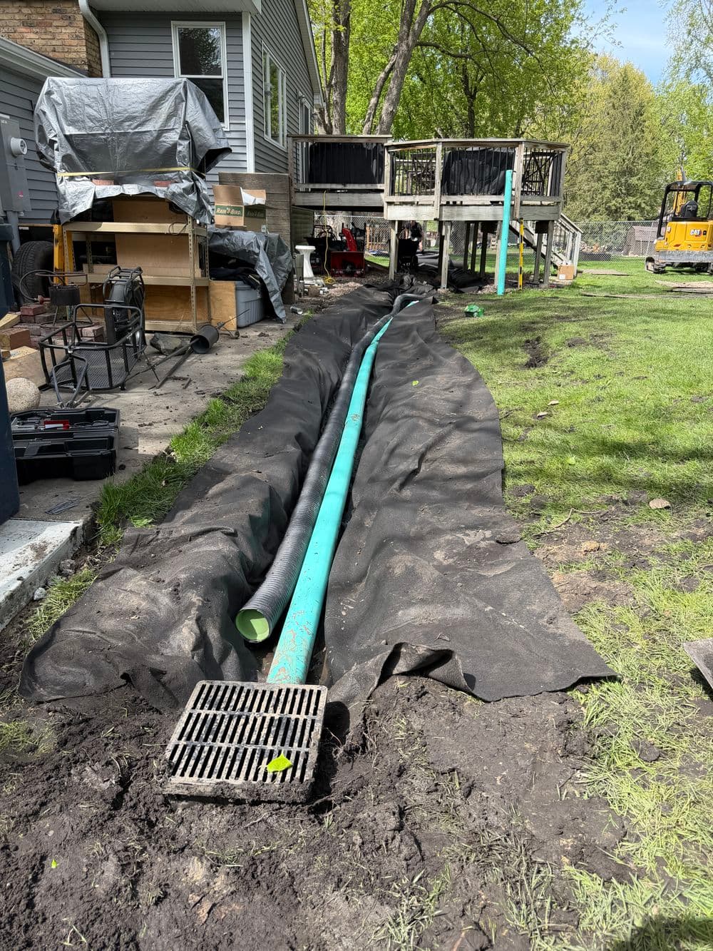 Drainage system installation with green pipes and gravel in a residential backyard.