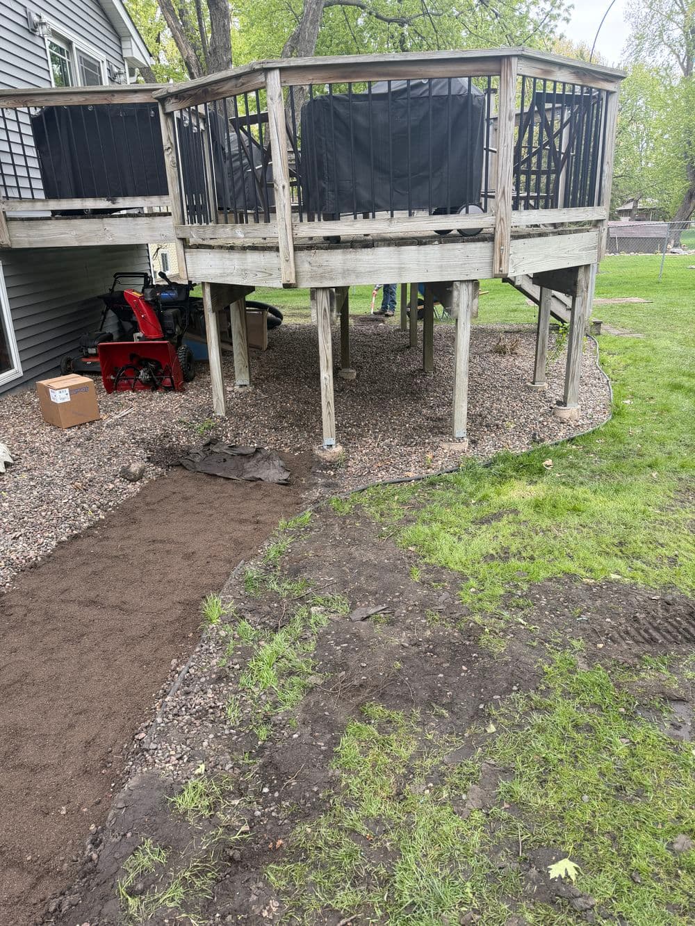 Backyard view of a wooden deck on stilts over gravel, with landscaping in progress below.